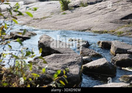 Ruisseau rocheux peu profond au-dessus des roches de granit. Image horizontale d'un ruisseau ensoleillé coulant dans un canyon de granit, des ondulations d'eau claire sur et autour de roches sombres. Banque D'Images