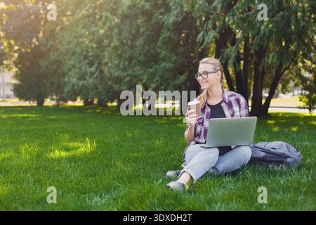 Femme utilisant un ordinateur portable et appréciant le café dans un parc vert pendant la journée Banque D'Images