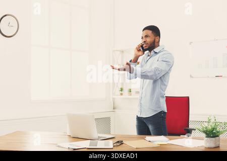 Homme d'affaires parle au téléphone dans le bureau tout en se tenant debout près du bureau Banque D'Images