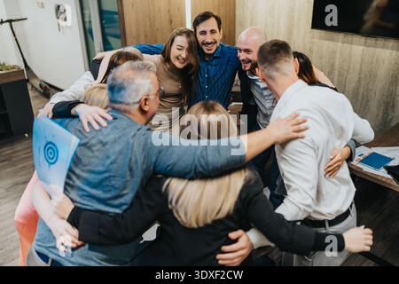 Des collègues et des amis diversifiés dans une joyeuse accolade de bureau, mettant en valeur le travail d'équipe, l'unité et la célébration Banque D'Images