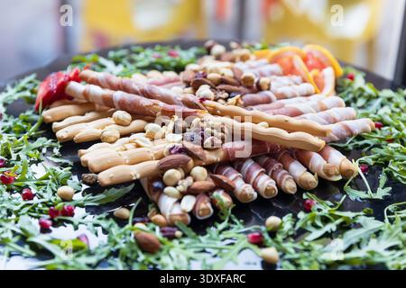 Plat de charcuterie élégant avec gressins enveloppés de prosciutto, noix mélangées, baies séchées et roquette fraîche, parfait pour la restauration, l'apéritif de fête Banque D'Images