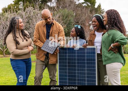 Famille afro-américaine tenant un grand panneau solaire et un petit panneau avec des câbles sur la pelouse. Photovoltaïque, multigénérationnel, renouvelable, durabilité, extérieur, park, parents || autorisation du modèle Banque D'Images