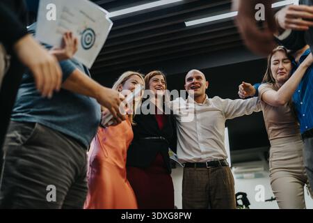 Groupe de collègues célébrant ensemble en cercle, souriant et levant la main dans l'unité Banque D'Images