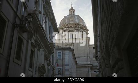 Dôme d'église en pierre au-dessus de la rue pavée étroite avec lanterne et drapeau italien accroché à la façade ; calme historique. Banque D'Images