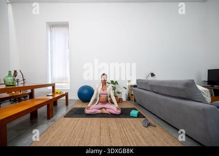 Femme enceinte méditant sur le tapis de yoga à la maison Banque D'Images