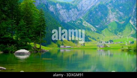 Paysage de montagne avec des arbres verts et de l'eau plate reflétant les maisons dans une vallée tranquille pendant la journée en été Banque D'Images