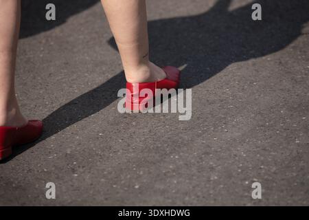 Femme dans les chaussures plates rouges marchant dans le marché, piéton marchant dans la lumière du soleil dure, vie de rue occupée, texture de peau de jambe, vue à angle élevé Banque D'Images