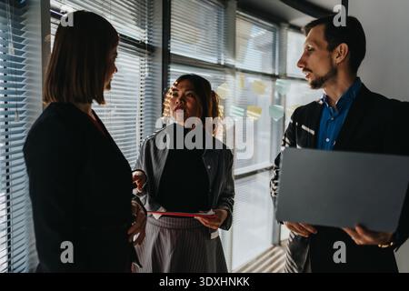Trois professionnels discutent des idées de projet dans un bureau moderne près d'une fenêtre avec des notes adhésives Banque D'Images
