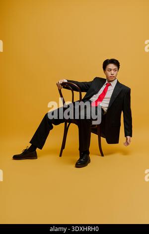 Un jeune homme d'affaires asiatique élégant dans un costume pointu et cravate rouge se dresse sur un fond animé. Banque D'Images