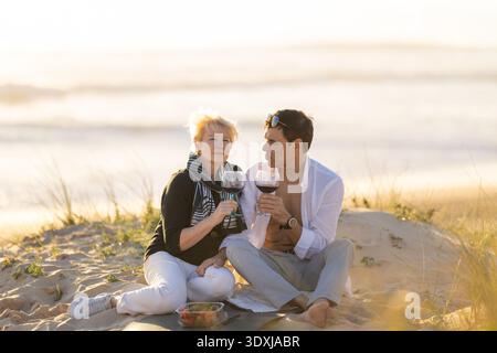Femme mature et homme appréciant le vin sur la plage pique-nique Banque D'Images