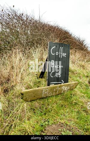 Un panneau rustique en bois écrit à la main sur une pente herbeuse annonce « Café, bacon, crabe » avec une flèche, tandis qu'une planche séparée en dessous indique « appât » Banque D'Images