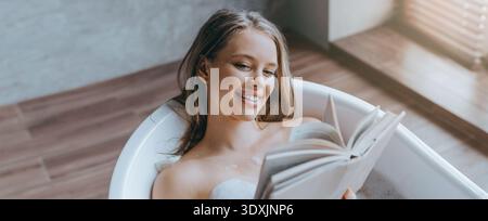 Détente dans une baignoire tout en lisant un livre dans une salle ensoleillée pendant la journée Banque D'Images