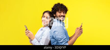 Jeune couple aime passer du temps ensemble tout en utilisant des smartphones sur un fond jaune Banque D'Images