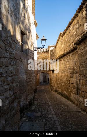 Ruelle pavée étroite avec murs en pierre, arche et lampadaire dans le centre historique de Baeza, Jaen, Andalousie, Espagne. Banque D'Images