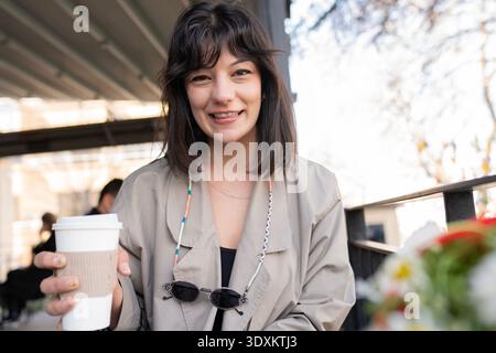 Jeune femme élégante tenant le café à l'extérieur dans un cadre urbain Banque D'Images