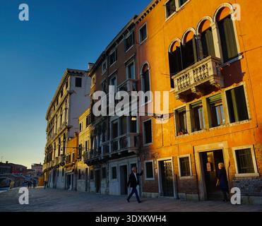 Les voisins se saluent dans la lumière dorée du soir sur les façades orange le long d'une calme fondamenta, Cannaregio, Venise, Italie Banque D'Images