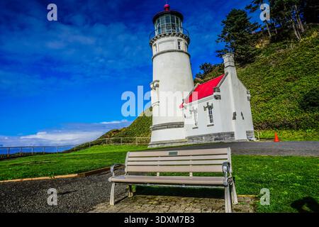 Un phare blanc se trouve sur une colline à côté d'un banc. Le banc est vide et le phare est entouré d'herbe Banque D'Images