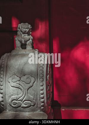 Une photographie détaillée en gros plan montre une cloche en pierre altérée avec des sculptures complexes, aux côtés d'un lion de pierre, reflétant le patrimoine architectural chinois Banque D'Images