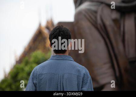 Homme faisant un vœu devant bouddha, personne anonyme en ville, franc moment de tous les jours, vue arrière Banque D'Images