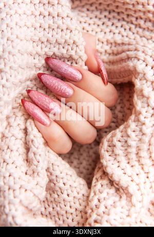 Main de femme arborant une manucure rose élégante avec un design complexe, reposant sur un pull confortable texturé Banque D'Images