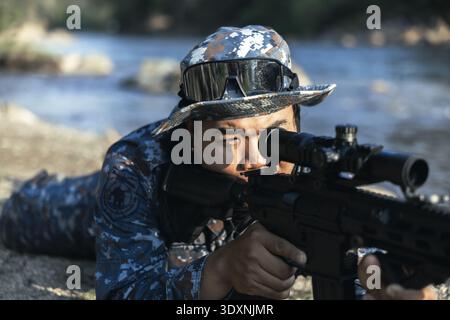 Soldat concentré en camouflage visant le fusil de sniper à l'extérieur. Cet homme déterminé, agent de la force spéciale, est prêt pour le combat en position couchée sur g Banque D'Images