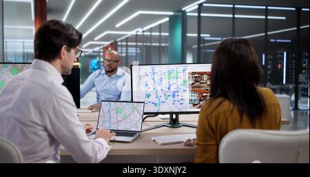L'équipe diverse étudie les cartes de ville sur les ordinateurs portables, la planification des terres et la propriété. Les gens qui travaillent ensemble utilisent le GPS et les ordinateurs Banque D'Images
