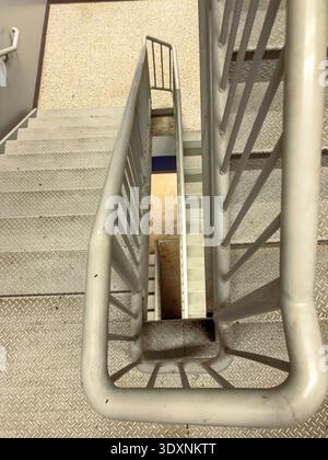 Une personne regarde du haut d'un escalier en métal avec des rampes. Les marches mènent au niveau inférieur d'un bâtiment. La lumière vient d'en haut, showi Banque D'Images