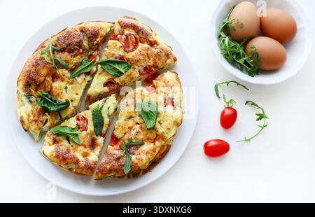Frittata cuite avec tomates cerises et épinards frais sur une table blanche. Plat d'été. Vue de dessus. Banque D'Images
