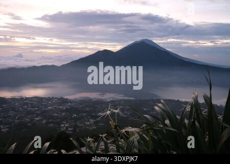 Majestueuse vue sur le lever du soleil sur le volcan actif Mont Batur, avec une mer de nuages remplissant la caldeira et le mont Agung visible au loin. Banque D'Images