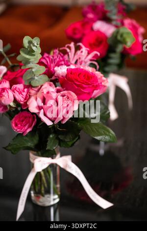 Bouquet rose avec eucalyptus dans un vase en verre sur une surface réfléchissante sombre Banque D'Images