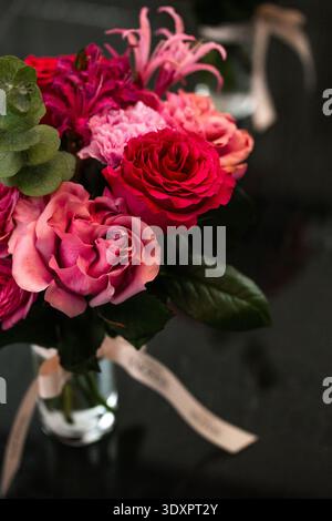Bouquet rose avec eucalyptus dans un vase en verre sur une surface réfléchissante sombre Banque D'Images