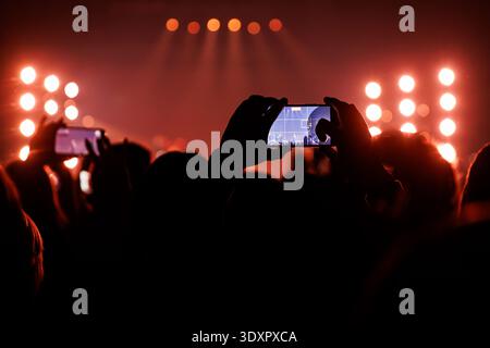 Silhouette d'une personne tenant un téléphone horizontalement pour enregistrer un spectacle avec des lumières rouges. Banque D'Images