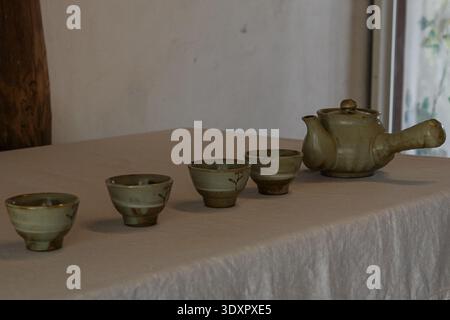 Une nature morte intérieure calme avec une théière en céramique traditionnelle et quatre tasses à thé assorties disposées en ligne sur une table recouverte de linge avec natura doux Banque D'Images