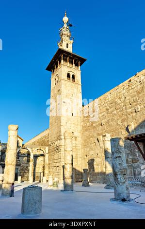Les gens marchent près de la mosquée omeyyade à Damas, explorant les murs de pierre et les structures anciennes sous un ciel bleu clair. Banque D'Images