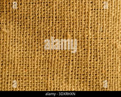 La texture grossière et tissée domine le cadre. Les tons naturels et terreux évoquent la simplicité rustique. Des teintes chaudes et dorées soulignent le grain du matériau. Par Banque D'Images