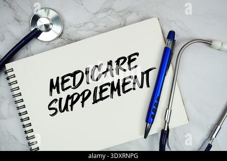 Texte du supplément Medicare écrit sur bloc-notes avec stéthoscope sur fond marbre Banque D'Images