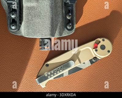 Gros plan du couteau pliant tactique et du pistolet avec compensateur dans l'étui sur la surface en cuir brun, tous les jours porter l'équipement EDC. Banque D'Images