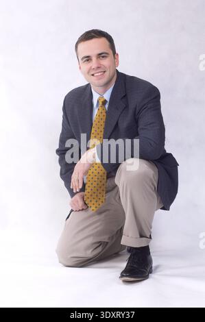Jeune homme exécutif agenouillé accroupissant portrait pleine longueur fond blanc, USA Banque D'Images
