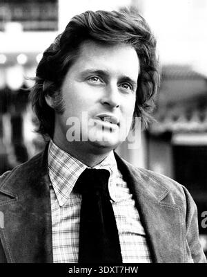 Cette publicité en noir et blanc datant de 1975 présente un portrait de Michael Douglas au début de sa carrière. On le voit regarder vers le haut, portant une chemise à carreaux et une cravate foncée, sous une veste en daim. Banque D'Images
