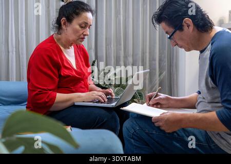 Femme tapant sur un ordinateur portable tandis que l'homme écrit sur un ordinateur portable, travaillant ensemble Banque D'Images