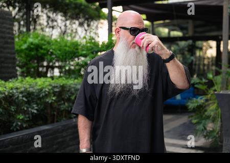 Old Bearded Bald Man buvant du café à l'extérieur dans un cadre urbain Banque D'Images