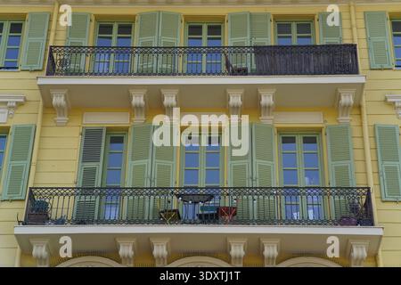 Façade jaune de bâtiment à Nice avec volets verts, balcons en fer forgé et mobilier de jardin sur la rue ensoleillée French Riviera.Nice, France Banque D'Images