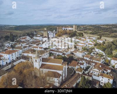 Vue aérienne du château médiéval, haut au-dessus du paysage, surplombant les bâtiments blanchis à la chaux aux toits en terre cuite, Óbidos, Leiria dis Banque D'Images