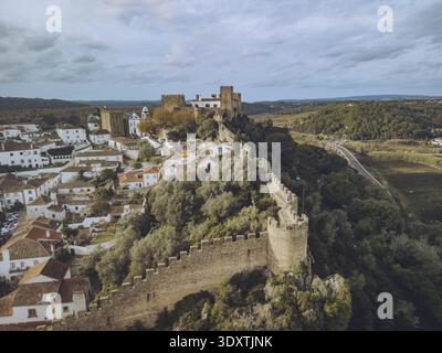 Vue aérienne des anciens murs de pierre embrassent le château historique, une tapisserie de toits en terre cuite nichée contre les collines verdoyantes, Óbidos, Leiria dis Banque D'Images