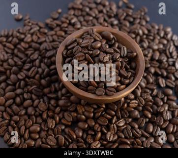 Un plan sophistiqué de grains de café torréfiés foncés. Un petit bol en bois rustique est rempli à ras bord de haricots et placé sur une surface sombre Banque D'Images
