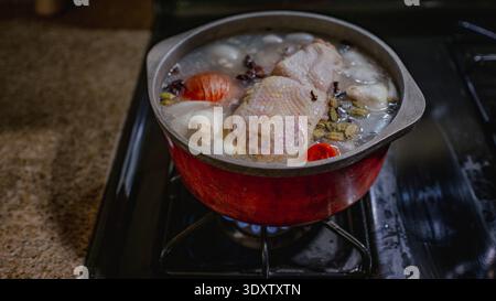 Un pot rouge se trouve sur une cuisinière à gaz, rempli d'eau, de morceaux de poulet Banque D'Images
