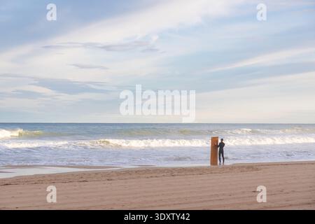 Une figure solitaire se tient sur la plage de sable de Torrevieja, en Espagne, regardant les vagues de l'océan se briser doucement tandis qu'un seul poteau en bois se dresse à proximité Banque D'Images