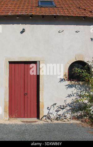 Porte de ferme rouge avec petit vélo enfant blanc appuyé contre le mur Banque D'Images