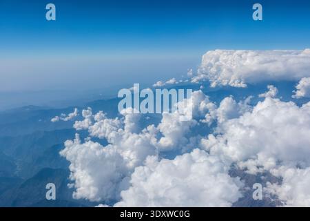 Vue aérienne des contreforts de l'Himalaya montrant une couche de nuages de cumulus blancs denses obscurcissant partiellement les crêtes sombres des montagnes ci-dessous. Banque D'Images