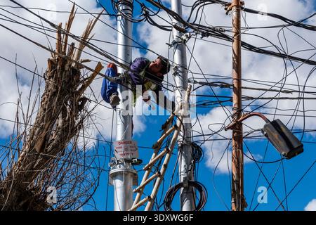 Un électricien travaille sur un enchevêtrement de lignes électriques aériennes au sommet d'un poteau de service à Leh, avec un panneau d'avertissement « danger 11000 volts » clairement visible. Banque D'Images